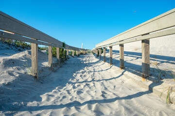 A Sandy Beach Path With a Wooden Fence on Each Side Casting Various Shadows