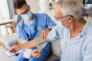 Male nurse measures blood pressure to senior man with mask while being in a home visit. - Powered by Adobe