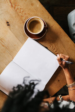 A woman sitting down at a coffee shop writing in a big journal / notebook