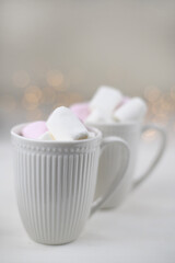 Hot winter drink with cocoa and marshmallows in mugs on wooden white background with Christmas garland. Top view.