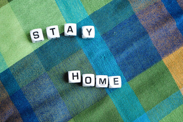 Words "Stay Home" formed with a set of letters on a green and blue plaid background