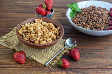Homemade granola with strawberry slices in a clay plate. On a wooden background. Vegetarian dish. Rustic style. Healthy breakfast.