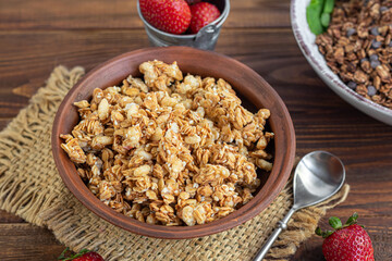 Homemade granola with strawberry slices in a clay plate. On a wooden background. Vegetarian dish. Rustic style. Healthy breakfast.