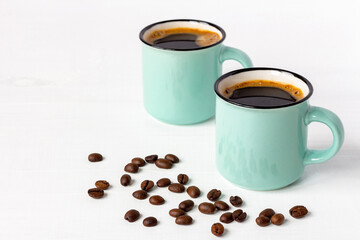Two mugs of fresh aromatic coffee with grains on white wooden background. Copy space