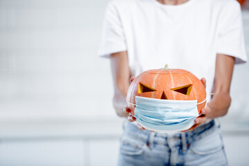 Celebration of halloween with medical mask concept. Pumpkin with a mask in white kitchen