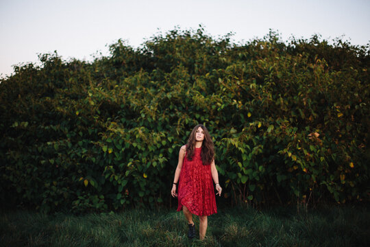 Young woman emerges from the bushes wearing a red dress