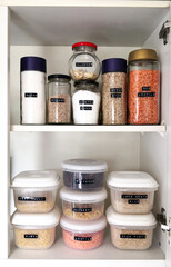The inside of a kitchen cupboard containing  dry food organised in transparent, labeled jars and...