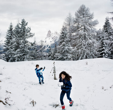 A girl and a boy playing in the snow in a beautiful mountan scenery