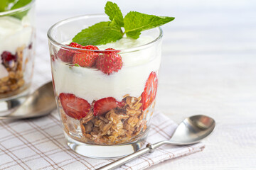 Homemade granola with slices of strawberries in transparent glasses on a light background. Vegetarian dish. Healthy breakfast.