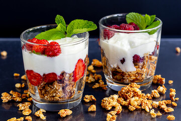Homemade granola with slices of strawberries in transparent glasses on a dark background. Vegetarian dish. Healthy breakfast.