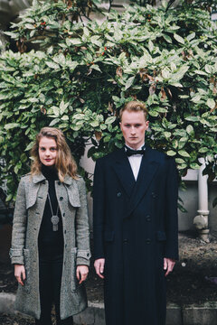 Young couple standing side by side in front of foliage