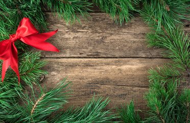 Christmas decorations made of pine branches and a red satin bow on a natural wooden background. Holiday background, top view. The concept of Christmas, New year.