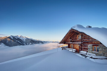 Snow covered mountain hut old farmhouse in the Austrian alps at sunrise against blue sky.