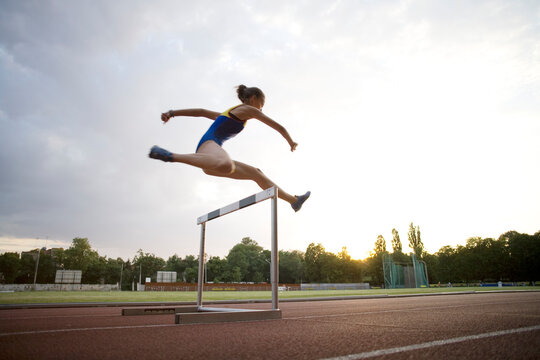 Young female hurdler training at dusk.