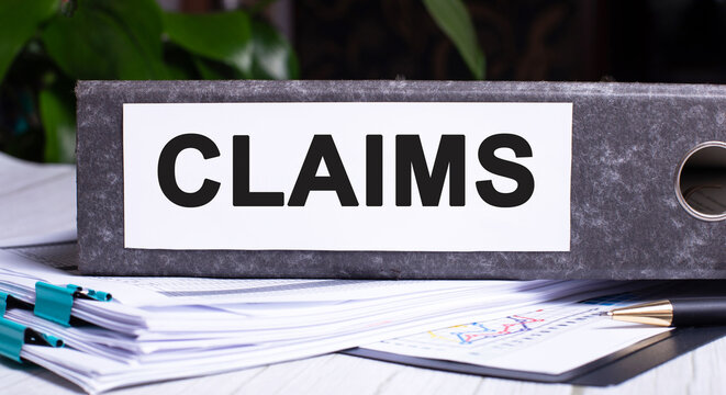 CLAIMS is written on a gray file folder next to documents. Business concept