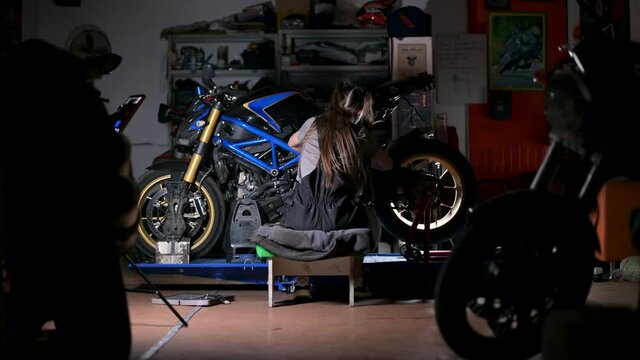 The camera zooms in on a young woman from behind. Woman enthusiastically repairs motorcycle in service