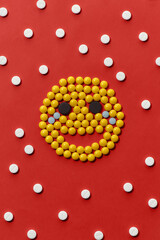 Top view of different colorful round pills lying in the shape of emoji, face isolated over red background. Health care and treatment concept.