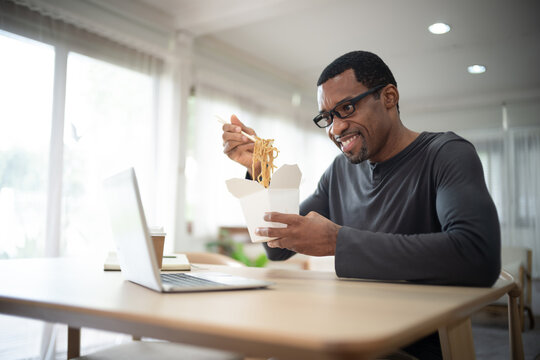 Handsome african american freelancer eating takeaway Asian food,spaghetti, with chopsticks.He online together with his friends on video call virtual party in quarantine time.Coronavirus outbreak 2020.