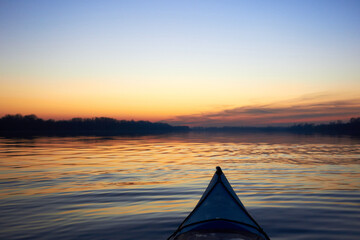 View from bow (prow) of blue kayak at colorful sunset over Danube river at autumn time