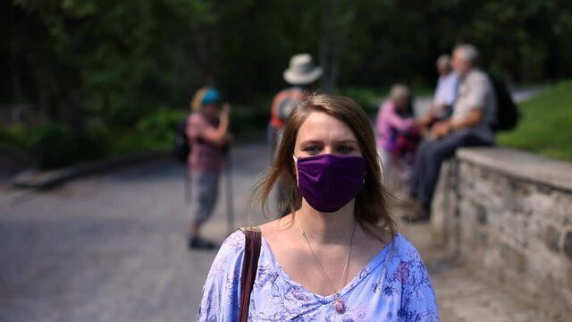 Beautiful young woman wearing covid-19 protective face mask to fight against coronavirus with a side bag walking on street