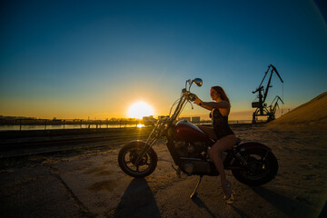 Red-haired woman in sexy lingerie in high heels sits on a motorcycle. Attractive red-haired girl sits on a motorcycle at sunset