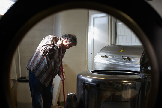 Mature man mopping the floor of the laundry in a textile workshop