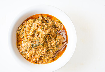 Egusi soup with beef in a white plate on a white background with negative space. Flatlay view