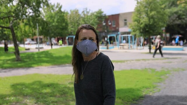 Young lonely woman wearing covid-19 face protection mask shield with pattern walking alone in park while looking around at nature