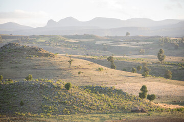A backlit landscape shot with slight mist and rolling hills.