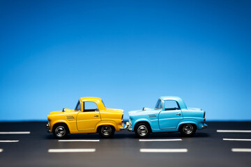 Two cars stand in a row on a road and a blue background.