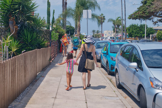 People Walking Down The Sidewalk Towards The Beach.