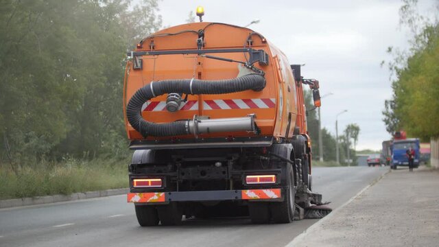 Big orange machine clears the asphalt with a sweeper - back view
