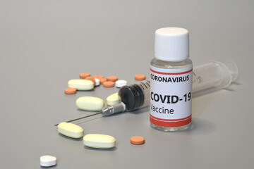 Detail of a syringe with vial containing Covid-19 virus vaccine and medicine pills isolated on gray background. Pharmaceutical research against Coronavirus, concept.