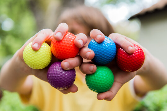 Child holds up colorful golf balls