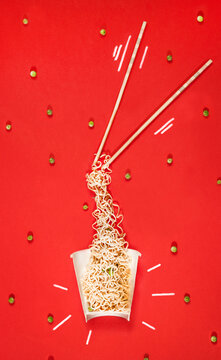 Cup with asian noodle/food with peas and chopsticks on red background.