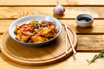 plate of soba with chicken and sesame seeds in teriyaki sauce on a wooden stand and sticks next to sesame seeds and soy sauce on a wooden table.