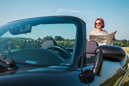 Woman looking a right road in the roadmap during her auto travel in the convertable cabriolet car. Traveling and navigation concept image.