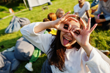 Fototapeta premium Young multi ethnic group of people watching movie at poof in open air cinema. Close up portrait of funny girl.