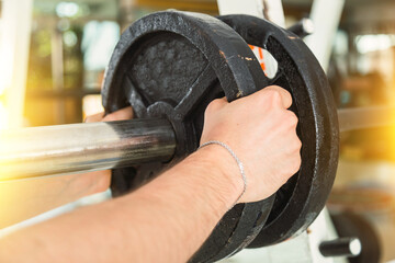 Men's hands in the gym.  Close up of adding weights on barbell.  Concept of sport and well-being.