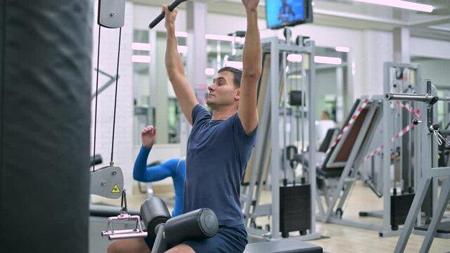 Side view of a woman trainer at a sports club who helps a young man to exercise on an exercise machine