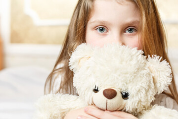 cute girl is lying with  soft toy on white bed