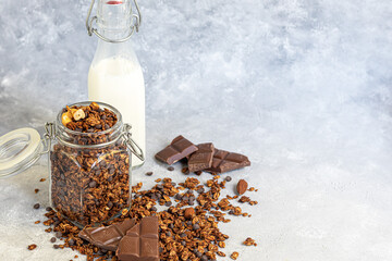 Homemade granola with strawberry pieces, chocolate and nuts in a glass jar. With the addition of milk or yogurt. On a gray background. Vegetarian dish.