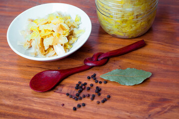 Jar of tasty sauerkraut on wooden table with peppermint and bay leaf, wooden spoon