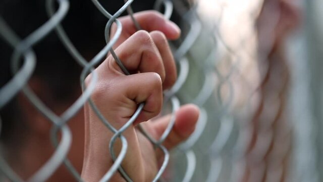 Person holding hands into metal fence outside, close-up black woman hand leaning on metallic wall gate