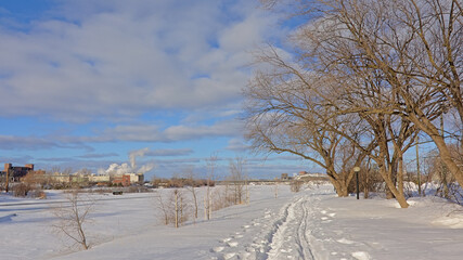 Snow covered walking pathway along Ottawa river, with industrial buildings of Hull district, Gatineau on the other side.