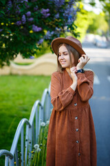Fototapeta premium Beautiful shapely long-haired girl in the hat on a background of lilac flowers