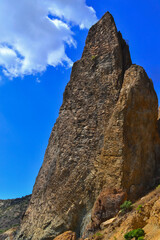 high sharp ancient basalt rock, Cape Fiolent stands on Black Sea coast, in the light of morning sun with shadows against the backdrop of blue sky with white cloud