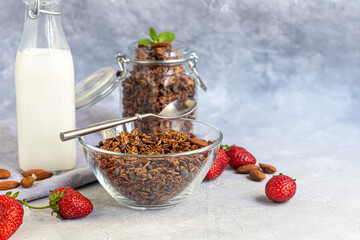 Homemade granola with strawberry pieces, chocolate and nuts in a glass jar. With the addition of milk or yogurt. On a gray background. Vegetarian dish.