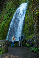Two hikers aretaking photos of Wahkeena falls, located in the Columbia River Gorge National Scenic Area.