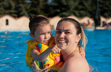 Mom and little daughter in the pool look into the distance. Girl points her finger at someone